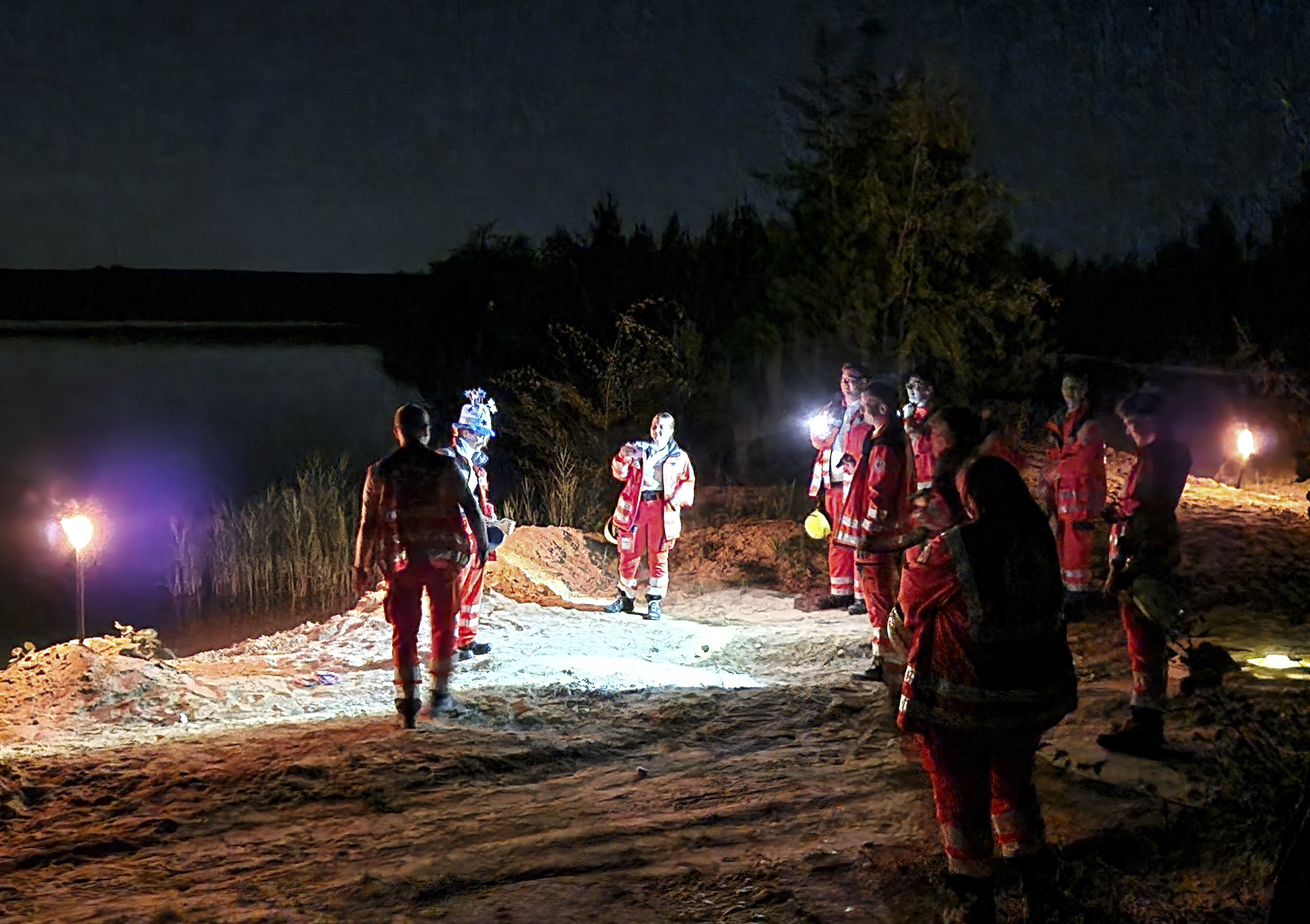 DRK-Einsatzkräfte bei nächtlicher Orientierungsübung, Fackeln und See im Hintergrund