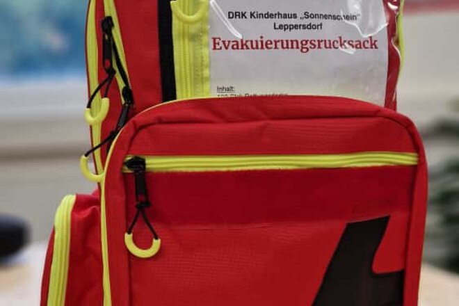 Roter Rucksack mit Aufschrift "Evakuierungsrucksack Kinderhaus Sonnenschein"