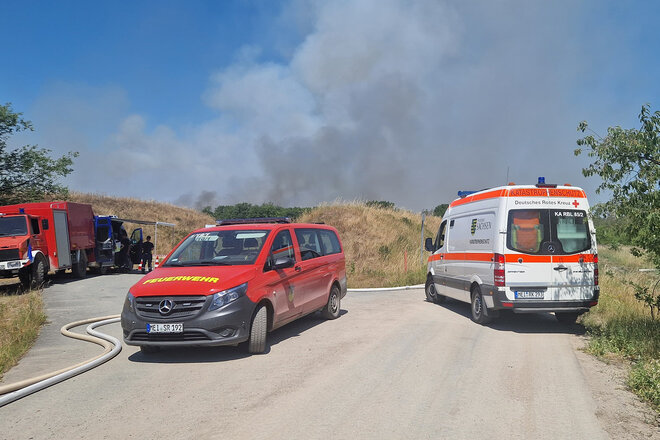 DRK-KTW und Feuerwehrfahrzeuge, im Hintergrund Rauchwolken